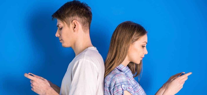 Photo of young man and woman standing back to back and texting on their cell phones Photo of young man and woman standing back to back and texting on their cell phones