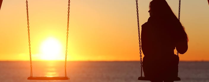 Silhouette of woman on swingset  overlooking ocean sunset. 