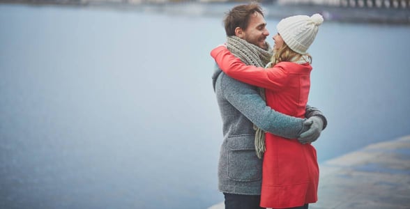 couple embracing in front of body of water