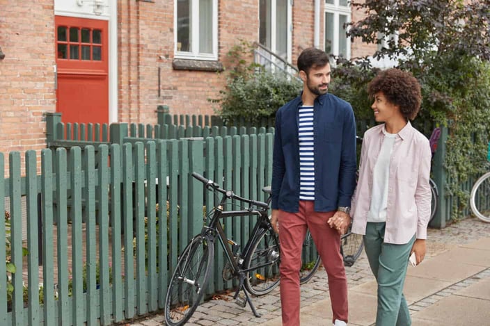View of romantic interracial couple hold hands, walk in rural setting, look positively at each other, bicycle near hence in background. View of romantic interracial couple hold hands, walk in rural setting, look positively at each other, bicycle near hence in background.