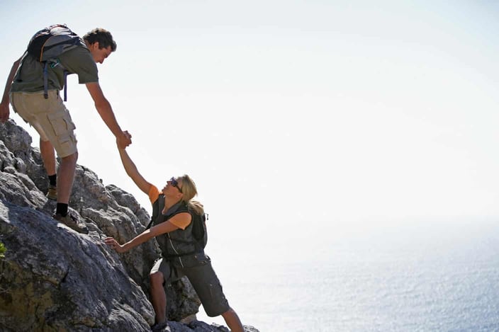 Man assisting woman as they rock climb together