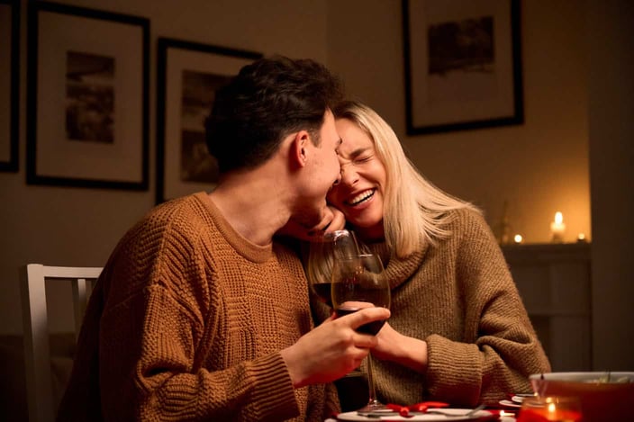 Happy young couple in love hugging, laughing, drinking wine, enjoying talking, having fun together celebrating Valentines day dining at home, having romantic dinner date with candles sitting at table. Happy young couple in love hugging, laughing, drinking wine, enjoying talking, having fun together celebrating Valentines day dining at home, having romantic dinner date with candles sitting at table.