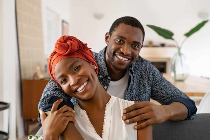 Portrait of mid adult happy african american couple hugging at home while sitting on couch. Portrait of mature man with his woman wearing traditional turban looking at camera. Black mid adult couple. Portrait of mid adult happy african american couple hugging at home while sitting on couch. Portrait of mature man with his woman wearing traditional turban looking at camera. Black mid adult couple.