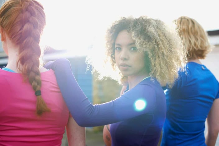 Rear view of three women exercising together with one woman looking at camera Rear view of three women exercising together with one woman looking at camera