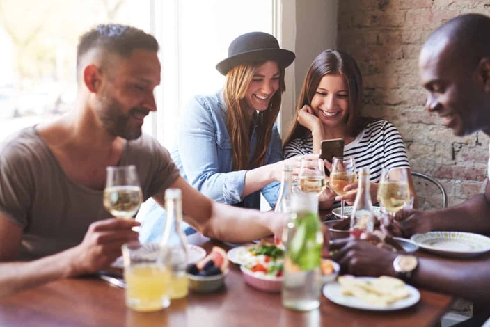 Group of two male and two female having delicious dinner while girls sharing something on phone. 
