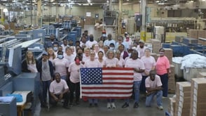 people stand in a factory behind an american flag