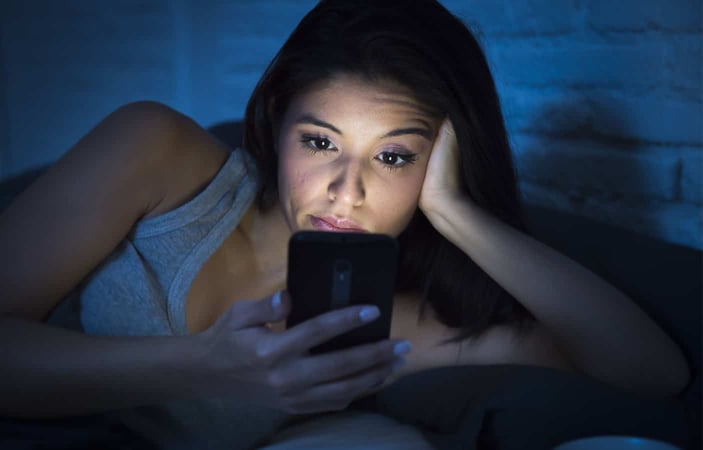 Photo of a woman frowning and looking at her cell phone in the middle of night Photo of a woman frowning and looking at her cell phone in the middle of night