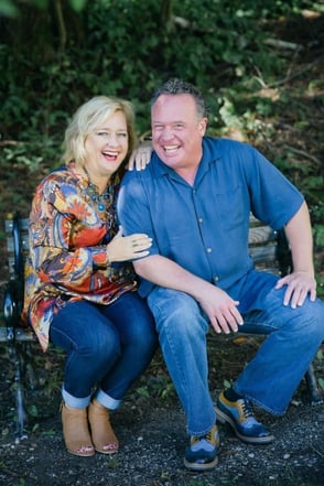 Jay and Laura Laffoon are sitting on a bench, Laura has her arms around Jay, they are smiling
