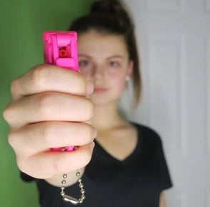 woman points pink pepper spray at camera