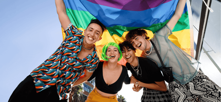 A group of young queer people celebrate with a rainbow flag at pride