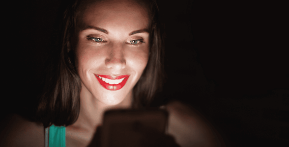 Woman in dark smiling at cellphone