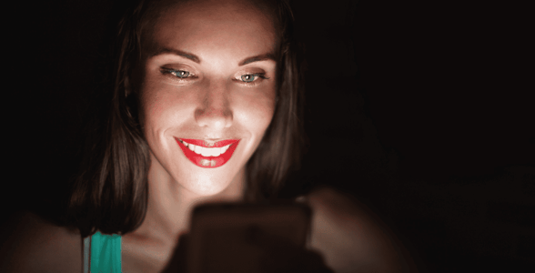 Woman in dark smiling at cellphone Woman in dark smiling at cellphone