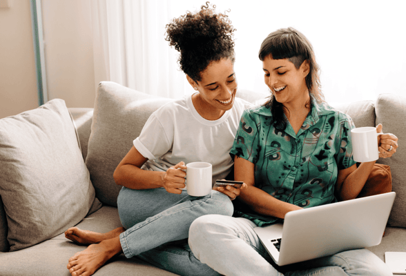 Queer women looking at a laptop together on the couch Queer women looking at a laptop together on the couch