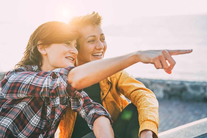 Two nonbinary people sitting close and looking out over a mountain Two nonbinary people sitting close and looking out over a mountain