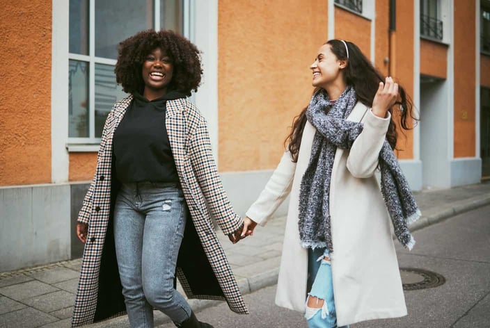 Interracial lesbian couple holding hands and laughing while walking Interracial lesbian couple holding hands and laughing while walking