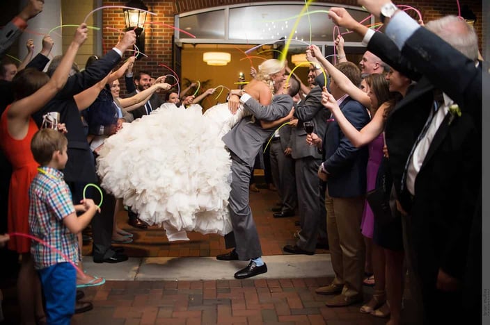 Bride being lifted up by groom between their wedding guests
