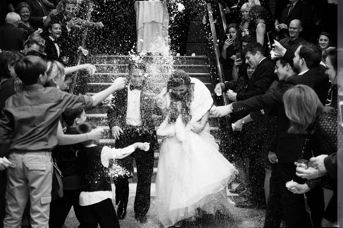 Black and white photo of a couple walking out of their wedding showered in champagne