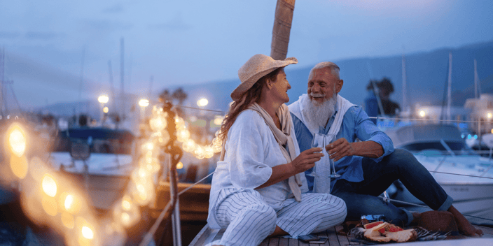 Senior couple clinking wine glasses on a boat with string lights
