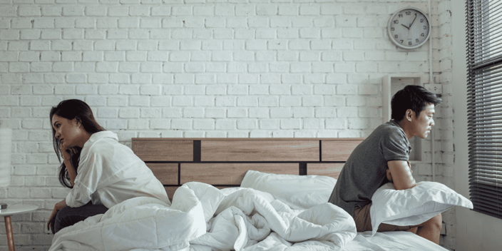 Asian couple sitting on bed facing away from each other upset