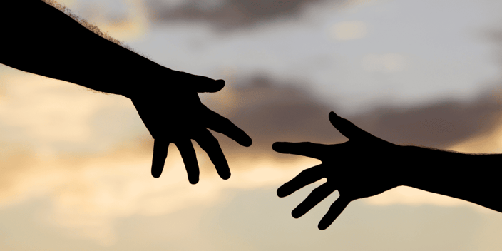 A man and woman's hands reaching out toward each other in front of clouds