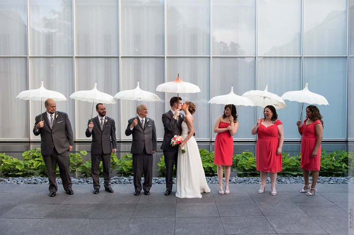 Bride and groom kissing in between line of their groomsmen and bridesmaids with umbrellas