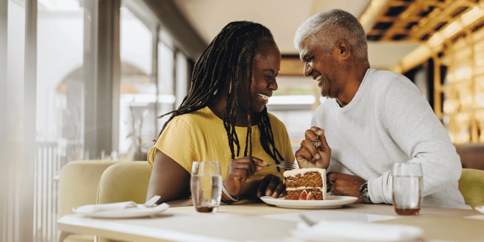 Older Black couple laughing at a coffee shop over cake