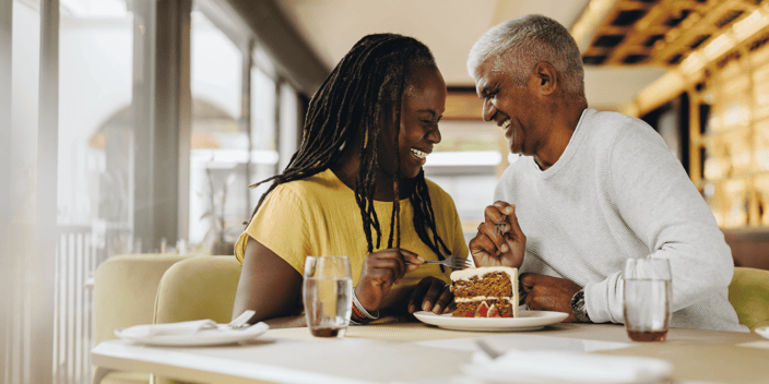 Older Black couple laughing at a coffee shop over cake Older Black couple laughing at a coffee shop over cake