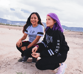 Sunshine City Counseling two women squatting on beach one with purple hair Sunshine City Counseling two women squatting on beach one with purple hair