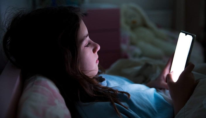 Photo of young girl looking at her cell phone in the dark