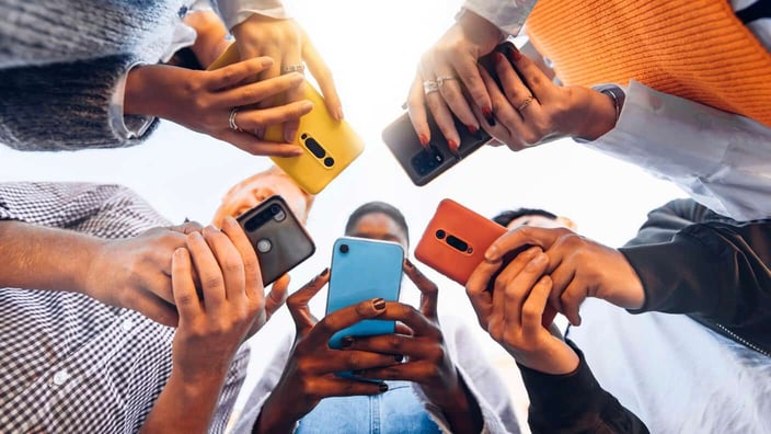 Photo of teens standing in a circle looking at their cell phones together