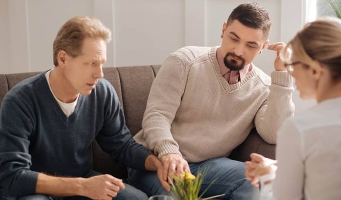 A photo of two men holding hands and talking with a therapist
