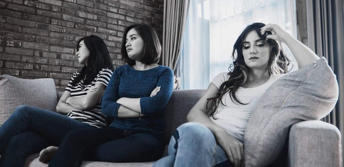 Group of three female friends sitting on couch. One member is being ostracized by the others, who are turned away from her. Group of three female friends sitting on couch. One member is being ostracized by the others, who are turned away from her.