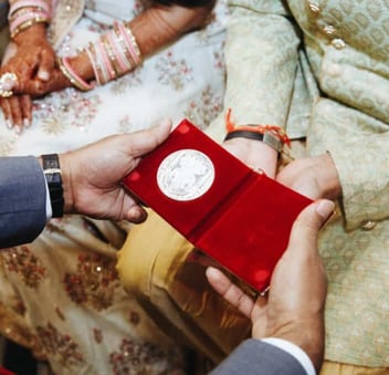A close up photo of a wedding guest giving an Indian bride and groom a present on their wedding day 