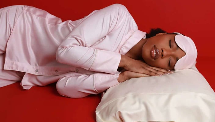 Photo of a young Black woman sleeping on a silk white pillow and wearing pink silk pajamas and a pink sleeping mask Photo of a young Black woman sleeping on a silk white pillow and wearing pink silk pajamas and a pink sleeping mask