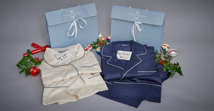 Photo of cream colored silk pajamas and navy colored silk pajamas gift set with cards that say for him and for her on top Photo of cream colored silk pajamas and navy colored silk pajamas gift set with cards that say for him and for her on top
