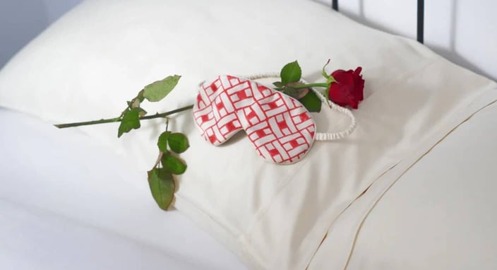 Photo of a red and white silk sleeping mask and a rose lying across a white silk pillowcase Photo of a red and white silk sleeping mask and a rose lying across a white silk pillowcase