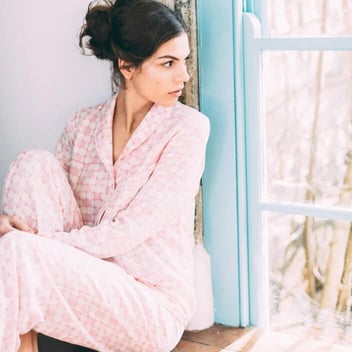 Photo of a young woman wearing pink and white patterned silk pajamas and looking out a window Photo of a young woman wearing pink and white patterned silk pajamas and looking out a window