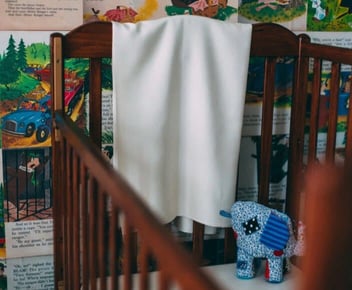 Photo of silk white baby blanket hanging over the side of a wooden crib Photo of silk white baby blanket hanging over the side of a wooden crib