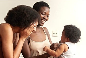 Photo of two moms holding and laughing with their baby Photo of two moms holding and laughing with their baby