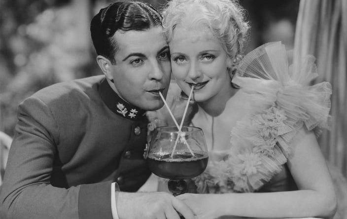 A photo of a vintage couple from the 1930s drinking from the same beverage with two straws A photo of a vintage couple from the 1930s drinking from the same beverage with two straws