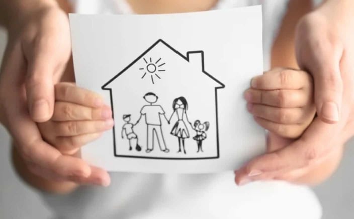 Photo of a little kid holding a drawing of a family standing in a house, and the parent's hands around the child's hands Photo of a little kid holding a drawing of a family standing in a house, and the parent's hands around the child's hands