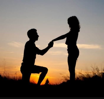 Photo of the silhouettes of a young man and woman as the man proposes 