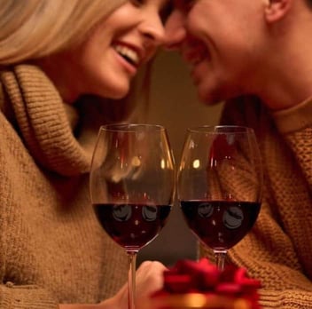 Close up photo of two glasses of wine held by a young couple smiling at each other 