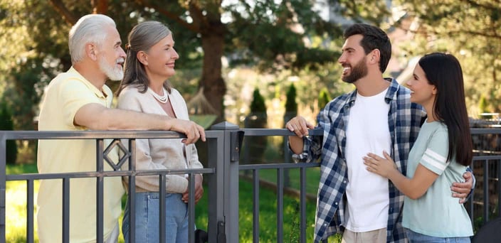 Older couple talking to younger couple across a metal fence.