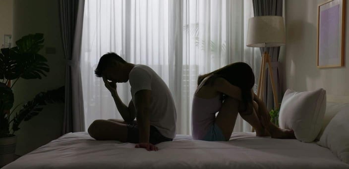 Couple on bed, looking away from one another.