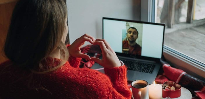 Woman on video call with man, making heart shape with her hands. Woman on video call with man, making heart shape with her hands.