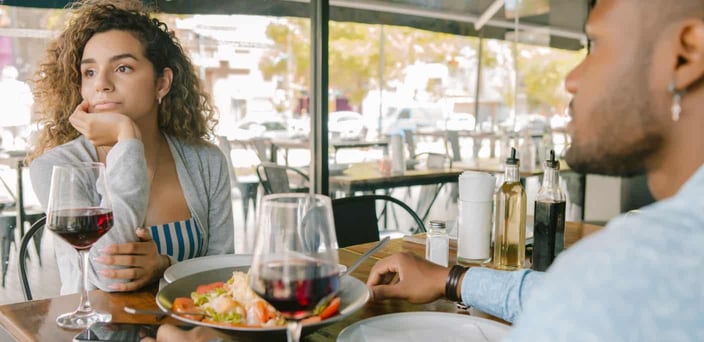Couple on an outdoor date. Woman is looking away, hand on chin, arms close to her chest.