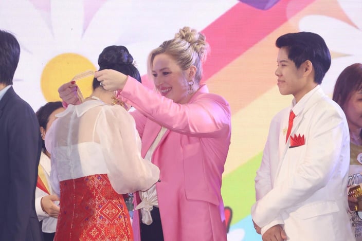 Tinder CMO Melissa Hobley smiling while putting a necklace around someone's neck and interacting with the LGBTQ couples