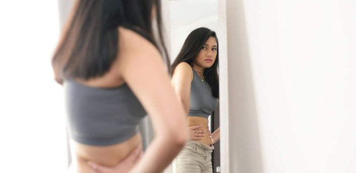 Woman looking at herself in the mirror, frowning Woman looking at herself in the mirror, frowning