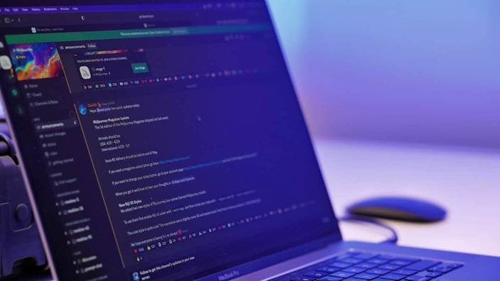 A close-up of a laptop displaying a Discord server interface with chat channels and messages, photographed in soft blue-purple lighting on a desk.